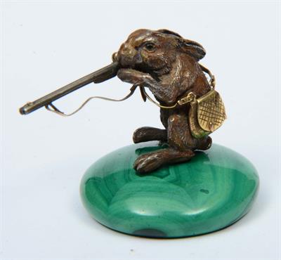 Lot 76 - A MINIATURE LACQUERED METAL MODEL of a hare holding a double barrelled shotgun and carrying a shooti