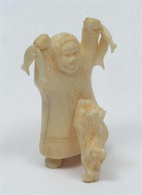 Lot 240 - AN ALASKAN INUIT MARINE IVORY CARVING of a man in a parka holding two fish with a dog leaping for th