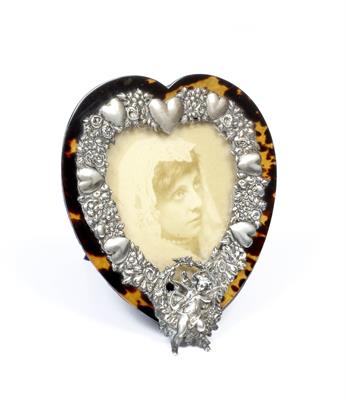 Lot 421 - A GEORGE V SILVER MOUNTED TORTOISESHELL HEART SHAPED PHOTOGRAPH FRAME the silver mounts decorated wi