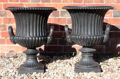 Lot 666 - A PAIR OF LATE 19TH CENTURY CAST IRON URNS with fluted bowls and masked handles (restored) 61cm high