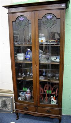 Lot 433 - AN ART NOUVEAU OAK BOOKCASE CABINET with twin glazed doors with stylised leaded flower head