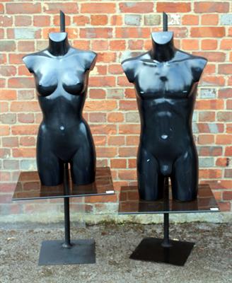 Lot 569 - A PAIR OF BLACK COMPOSITE TORSO MANIKINS each on a glass shelf and with a black painted adjustable