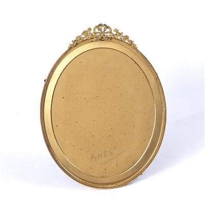 Lot 139 - A GILT METAL OVAL PORTRAIT FRAME with ribbon swag cresting and easel support