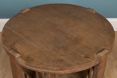 Lot 4 - A Cotswold school limed oak circular occasional table with bookcase beneath