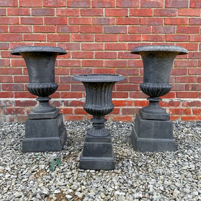 Lot 1409 - A pair of campana cast iron urns on plinths, and a further smaller urn